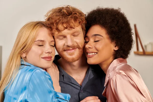 Polygamy lovers, portrait of happy man with red hair and multicultural women, cultural diversity, non traditional partners, freedom in relationship, acceptance and understanding, closed eyes — Stock Photo
