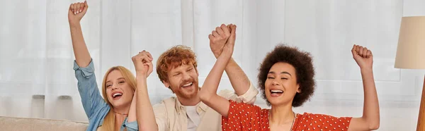 Polyamorous relationship, cultural diversity, redhead man raising hands with multiracial female lovers, positivity, freedom and acceptance, love triangle, people in open relationship, banner — Stock Photo