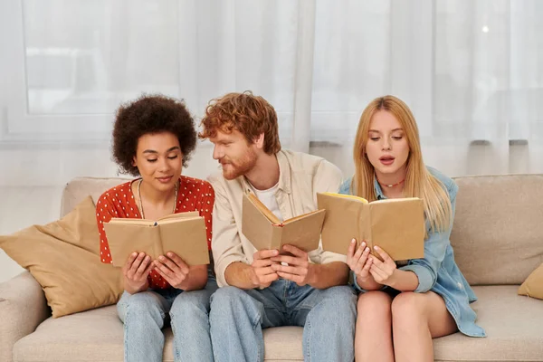 Alternative relationships, polygamy concept, intelligent multicultural women reading books with redhead boyfriend in living room, modern family, hobby and leisure, freedom in relationship — Stock Photo