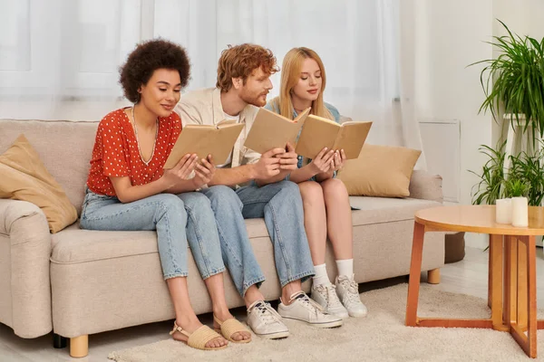 Relationship diversity, polygamy concept, intelligent multicultural women reading books with redhead boyfriend in living room, modern family, hobby and leisure, freedom in relationship — Stock Photo