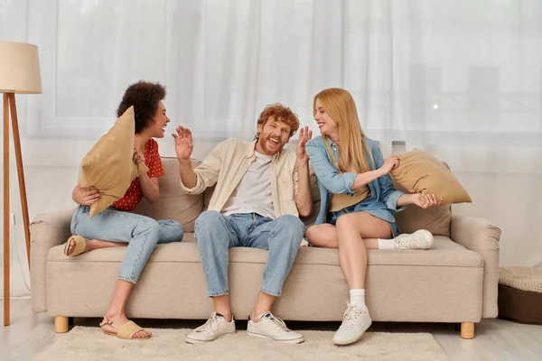 Polygamy, group relationship, happy multicultural women and bearded man fighting with pillows, open relationship, diversity and bonding, non monogamy, three people having fun — Stock Photo