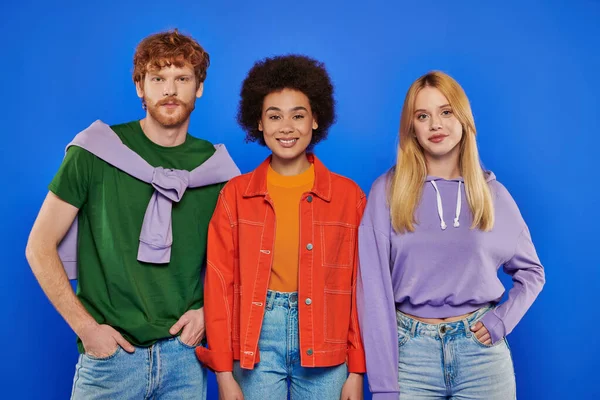 Polyamory concept, cheerful multicultural women and redhead man looking at camera on blue background, studio photography, cultural diversity, polygamy, modern family, colorful clothes — Stock Photo