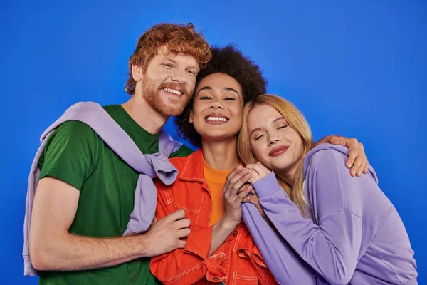 Polyamory relationships, positive multiracial women and redhead man looking at camera on blue background, studio photography, cultural diversity, polygamy, modern family, colorful attire — Stock Photo