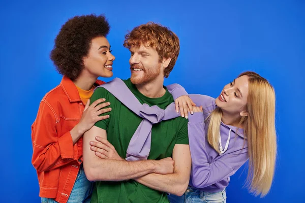 Acceptance, alternative relationships, polyamory, three people, young redhead man and beautiful multiracial women on blue background, studio shot, vibrant colors, stylish attire, modern family — Stock Photo