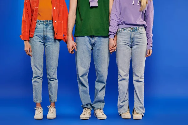 Альтернативна сім'я, полігамія, частковий погляд на поліаморію три людини, молодий чоловік і жінки тримають руки на синьому фоні, студійний знімок, яскравий одяг, романтичні, сучасні відносини — стокове фото