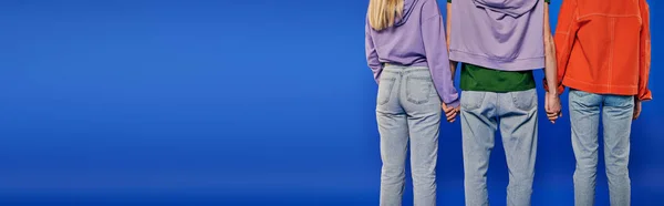 Polygamy, back view of polyamory three people, young man and women holding hands on blue background, studio shot, denim fashion, love triangle, cropped shot, bonding, banner — Stock Photo