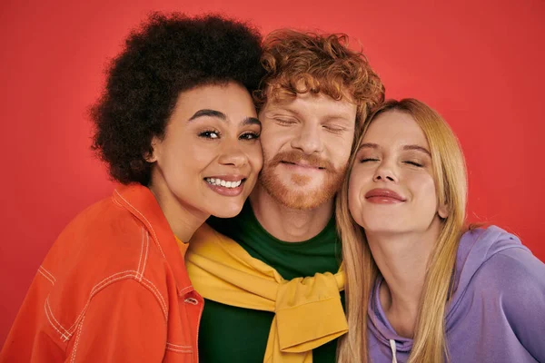Polyamorous concept, portrait of young man and multicultural women on coral background, studio shot, vibrant colors, love triangle, bonding and acceptance, happy polygamy lovers — Stock Photo
