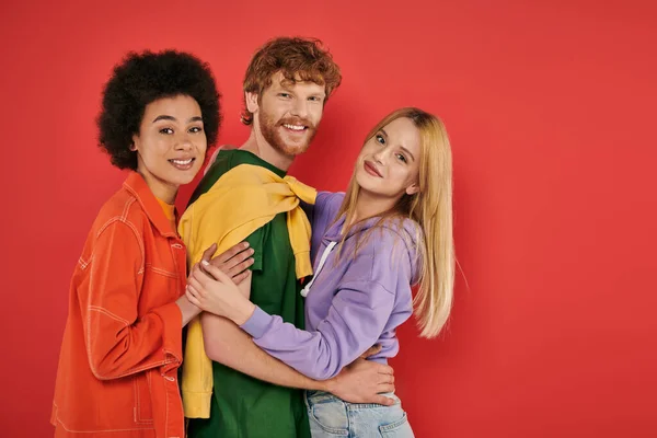 Open relationship, polygamy concept, three interracial lovers hugging each other on coral background, cultural diversity, polyamorous, happy multiethnic people looking at camera — Stock Photo