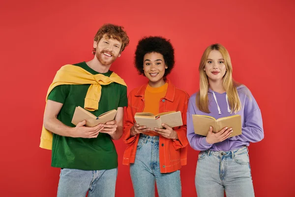 Polygamy concept, interracial people reading books on coral background, cultural diversity, polyamorous, happy multiethnic lovers in open relationship, intelligent and cheerful, looking at camera — Stock Photo