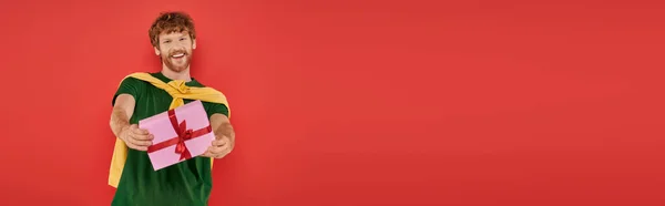 Célébration, homme rousse heureux avec barbe posant en tenue décontractée sur fond corail, tenant boîte cadeau, occasions festives, cadeau enveloppé, mode et tendance, style urbain, vacances, bannière — Photo de stock