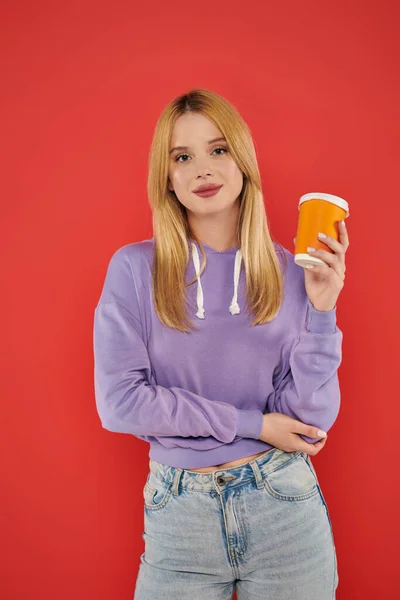 Takeaway drink, youthful fashion, blonde young woman in casual attire holding paper cup on coral background, happiness, looking at camera, vibrant colors, fashion forward, hot beverage — Stock Photo