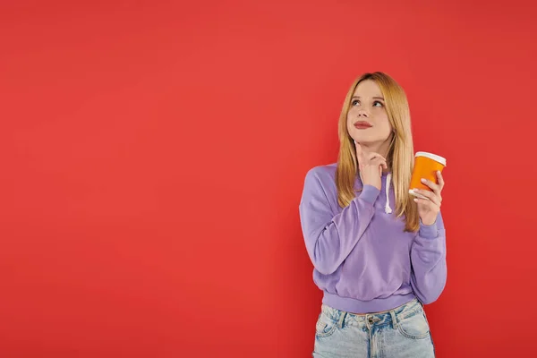 Hot beverage, youthful fashion, blonde young woman in casual attire holding paper cup on coral background, happiness, looking away, vibrant colors, fashion forward, takeaway drink — Stock Photo
