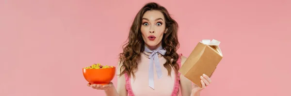 Housewife concept, shocked young woman posing like a doll, holding takeaway food and bowl with corn flakes, pink background, conceptual photography, home duties, emotional, banner — Stock Photo