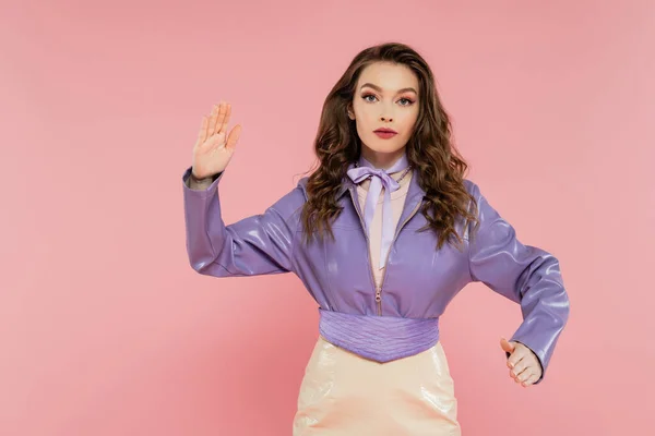 Glamour, attractive young woman with wavy hair gesturing and looking at camera, pretending to be a doll, trendy outfit, model in purple jacket posing on pink background, studio shot, conceptual — Stock Photo