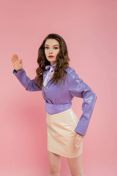 Doll concept, beautiful young woman with wavy hair gesturing and looking at camera, trendy outfit, brunette model in purple jacket posing on pink background, studio shot, conceptual — Stock Photo