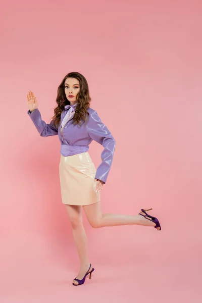 Doll pose, beautiful young woman with wavy hair gesturing and looking at camera, trendy outfit, brunette model in purple jacket and high heels posing on pink background, studio shot, conceptual — Stock Photo