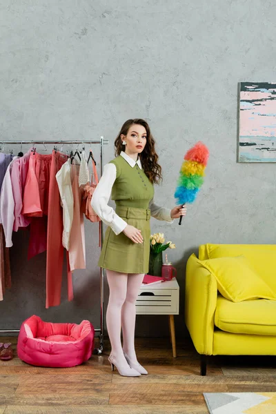 Housekeeping concept, young woman with brunette wavy hair holding dust brush, housewife looking at camera and doing her daily duties, lifestyle, domestic chores, acting like a doll, tidy home — Stock Photo