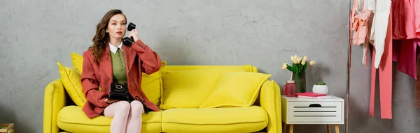 Llamada telefónica, mujer atractiva con el pelo ondulado sentado en el sofá amarillo, ama de casa hablando por teléfono retro, posando como una muñeca, mirando hacia otro lado, interior moderno, sala de estar, pancarta - foto de stock