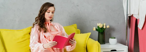 Konzeptfotografie, Frau mit brünetten welligen Haaren, häusliches Leben, attraktive Hausfrau liest Buch, sitzt auf gelbem Sofa, komfortables Wohnen, häuslicher Lebensstil, Banner — Stockfoto