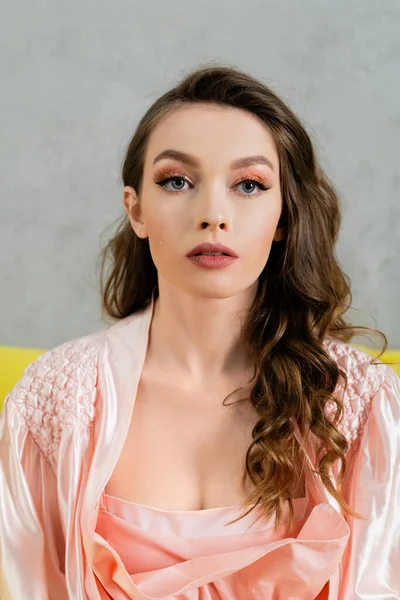 Ritratto di bella giovane donna con i capelli ondulati bruna guardando la macchina fotografica, headshot, vestaglia rosa, casalinga con trucco serale, concetto di bambola, gioventù femminile — Foto stock