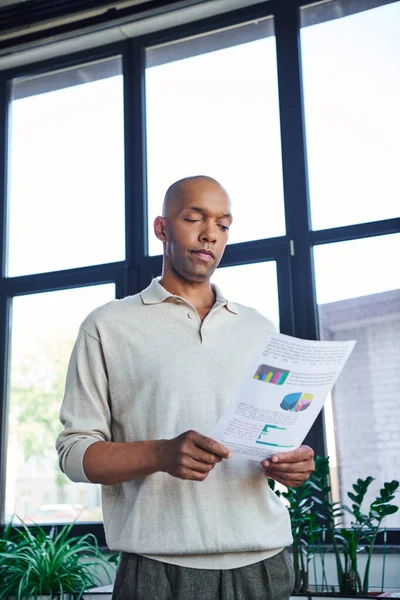 Myasthenia gravis, bold african american businessman with eye syndrome looking at graphs, muscular disorder, corporate culture, dark skinned office worker with chronic illness near windows — Stock Photo
