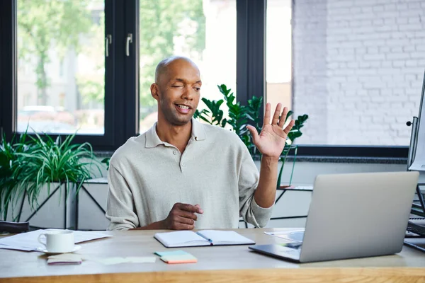 Miastenia gravis, negrito empresário afro-americano com síndrome do olho acenando a mão durante videochamada no laptop, trabalhador de escritório de pele escura com síndrome da ptose, diversidade e inclusão — Fotografia de Stock