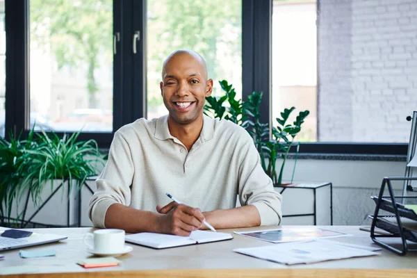 Чоловік з птозом приймає нотатки, щасливий афроамериканський бізнесмен дивиться на камеру, щасливий темношкірий офісний працівник з хворобою міастенії, різноманітністю та включенням — стокове фото