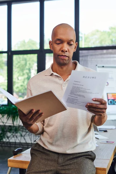 Dark skinned man with myasthenia gravis disease holding resume and folder, bold african american office worker with ptosis eye syndrome, inclusion, graphics on background — Stock Photo
