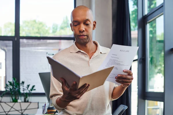 Dark skinned man with myasthenia gravis disease holding resume and looking at folder, bold african american office worker with ptosis eye syndrome, inclusion and diversity — Stock Photo