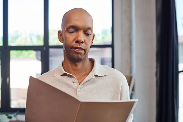 Portrait of dark skinned man with myasthenia gravis disease holding folder,  bold african american office worker with ptosis eye syndrome, inclusion, neurological disorder, professional headshots — Stock Photo