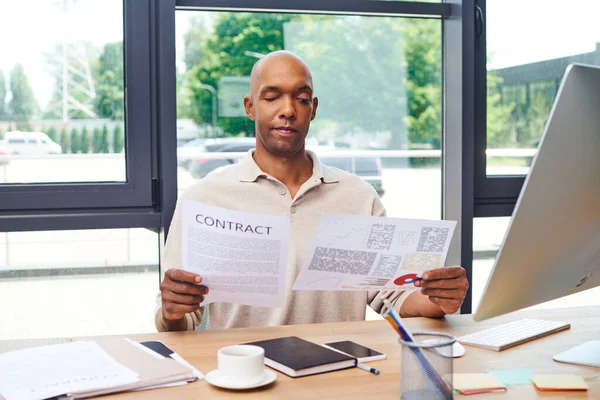 Inclusion, african american man with myasthenia gravis disease holding contract, dark skinned office worker in casual attire working at desk, smartphone, cup of coffee and stationery, monitor — Stock Photo
