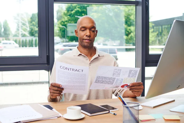 Inclusão, homem americano africano com miastenia gravis doença segurando contrato, trabalhador de escritório de pele escura em traje casual trabalhando na mesa, smartphone, xícara de café e papelaria, monitor — Fotografia de Stock