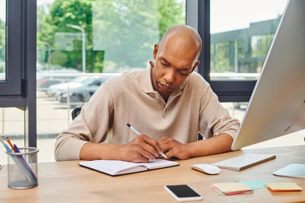 Inclusion, african american man with myasthenia gravis at work, bold and dark skinned office worker taking notes, corporate culture, monitor and smartphone, computer mouse and keyboard on desk — Stock Photo