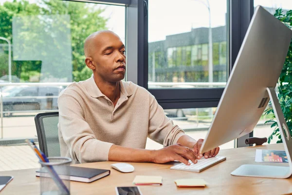 Inclusion, african american man with myasthenia gravis at work, bold and dark skinned office worker typing on keyboard and using computer, looking at monitor, smartphone and stationery on desk — Stock Photo