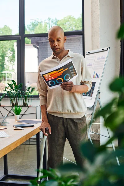 Diversité et inclusion, personnes réelles, homme afro-américain audacieux avec myasthénie grave, employé de bureau à la peau foncée debout avec canne à pied et graphiques, maladie chronique — Photo de stock