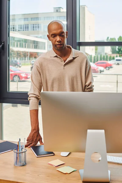 Myasthenia gravis syndrome, bold african american businessman with ptosis syndrome looking at computer monitor, dark skinned office worker in casual attire standing at desk, inclusion — Stock Photo