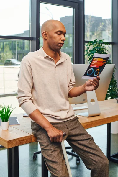 Inclusion, myasthenia gravis syndrome, bold african american businessman standing with walking cane and looking at charts near computer monitor, dark skinned office worker in casual attire — Stock Photo