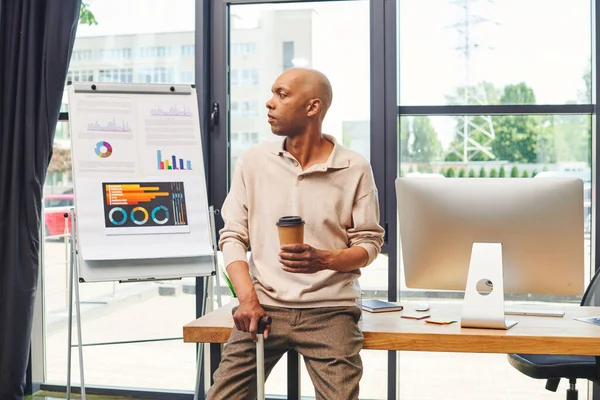 Inclusion, myasthenia gravis syndrome, bold african american man standing with walking cane and to go coffee, computer monitor, dark skinned office worker in casual attire — Stock Photo