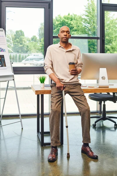 Inclusion, myasthenia gravis syndrome, bold african american man standing with walking cane and coffee to go, computer monitor, dark skinned office worker in smart casual attire — Stock Photo