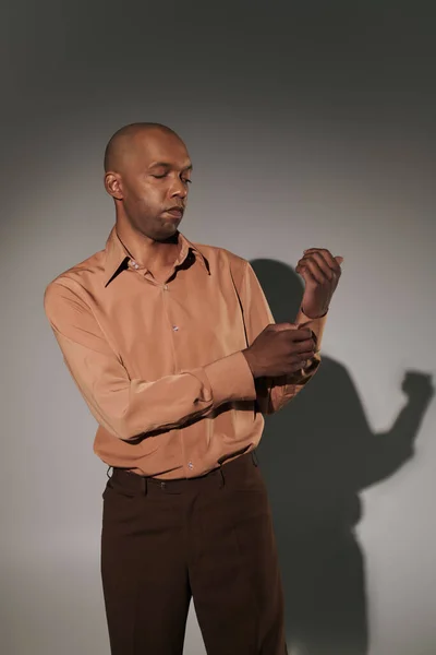 Реальні люди, сміливий афроамериканський чоловік з міастенією, що стоїть на сірому фоні, темношкіра людина регулює рукав у сорочці, розумний випадковий, різноманітність та включення, фізичні пошкодження — стокове фото