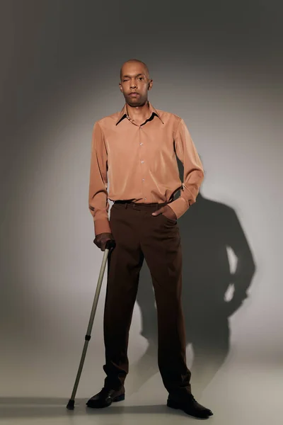 Real people, bold african american man with myasthenia gravis standing with walking cane on grey background, hand in pocket, pose, dark skinned person in shirt, diversity and inclusion, full length — Stock Photo