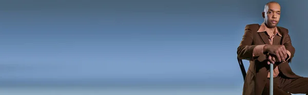 Diversidade e inclusão, homem afro-americano com síndrome da miastenia gravis sentado na cadeira e olhando para a câmera em fundo azul, apoiando-se na bengala, dificuldade em andar, ptose, banner — Fotografia de Stock
