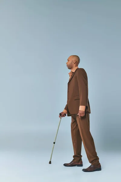 Vraies personnes, vue complète de l'homme afro-américain avec myasthénie gravis appuyé sur la canne à pied sur fond gris, personne à la peau foncée en costume, la diversité et l'inclusion — Photo de stock