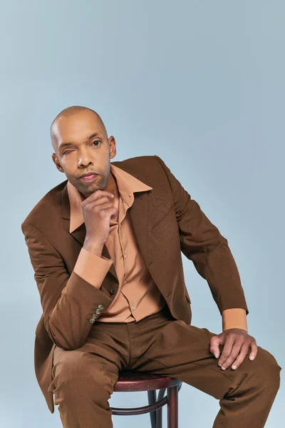 Real people, portrait of african american man with myasthenia gravis sitting on wooden chair on grey background, dark skinned person in suit looking at camera, diversity and inclusion — Stock Photo