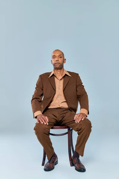 Vraies personnes, pleine longueur de gras homme afro-américain avec myasthénie gravis assis sur une chaise en bois sur fond gris, personne à la peau foncée en costume regardant la caméra, la diversité et l'inclusion — Photo de stock