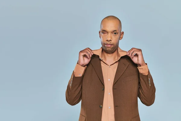 Eye syndrome, physical impairment, bold african american man with myasthenia gravis standing on grey background, dark skinned person in formal wear adjusting collar of shirt, diversity and inclusion — Stock Photo