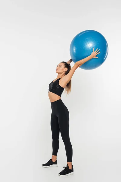 Fit sportswoman in active wear and sneakers holding fitness ball and training on white background — Stock Photo