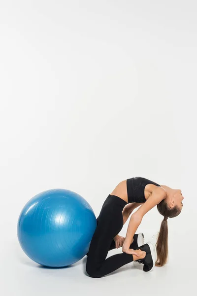 Femme en noir porter actif étirement près de balle de fitness sur fond blanc, concept de santé et de remise en forme — Photo de stock