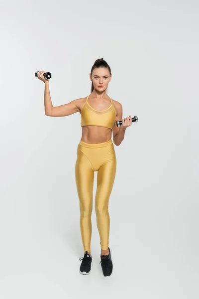 Mujer en entrenamiento de ropa deportiva con mancuernas sobre fondo blanco, fuerza y concepto de determinación - foto de stock