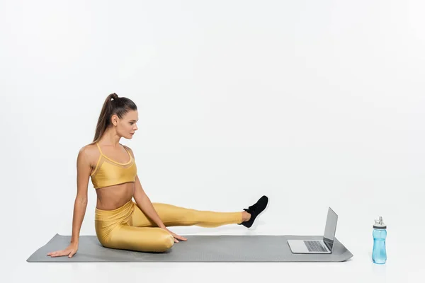 E-sports, woman in sportswear sitting near laptop and bottle on fitness mat, white background — Stock Photo